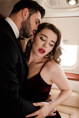 Yakışıklı adam uçakta seksi, zarif kadını kucaklıyor.
