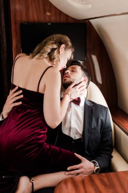 Yakışıklı adam, uçakta kucağında oturan seksi, zarif kadını kucaklıyor.