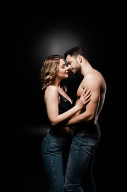 Siyah arka planda sarılan seksi gömleksiz bir adam ve sütyenli güzel bir kız.