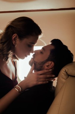 Uçakta yakışıklı bir adamın yüzüne dokunan seksi genç kadının yan görüntüsü.