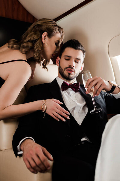sensual woman touching elegant man holding glass of champagne in plane