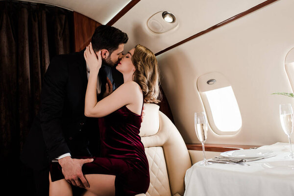 handsome man touching leg and kissing seductive woman in plane