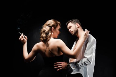 Elinde sigara tutan seksi, zarif bir kadın ve siyah giyinmiş yakışıklı bir adam.