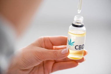 selective focus of woman holding pipette and bottle with cbd lettering  clipart