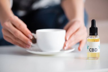 CBD harfli, şişenin yanında çay içen olgun bir kadın görüntüsü.