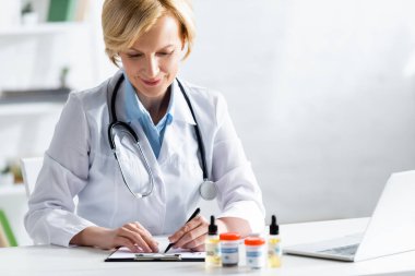 Tıbbi esrar ve cbd içeren şişelerin yanında reçete yazan neşeli ve olgun doktorların seçici odağı 