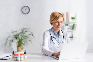 Tıbbi esrar ve CD harfleri olan şişelerin yanında dizüstü bilgisayar kullanan olgun bir doktor. 