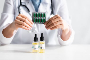 Beyaz önlüklü doktorun elinde şişelerin yanında CBD harfleri olan haplarla dolu su topladığı görüntüler. 