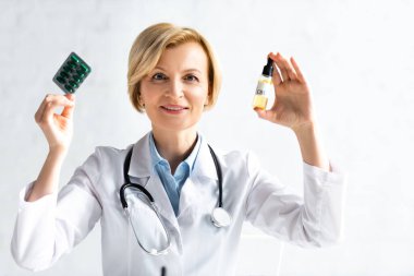 Beyaz önlüklü, mutlu ve olgun bir doktor. Elinde bir şişe cd kartonpiyer ve klinikte de haplar var. 