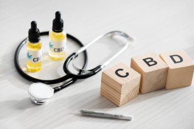 Tahta küplerin, kalemlerin ve steteskopların yanında cbd harfleri olan şişelerin seçici odak noktası 