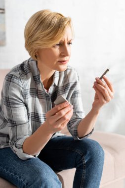 Olgun bir kadının kanepede otururken esrar ve çakmakla esrar içtiği seçici odak noktası