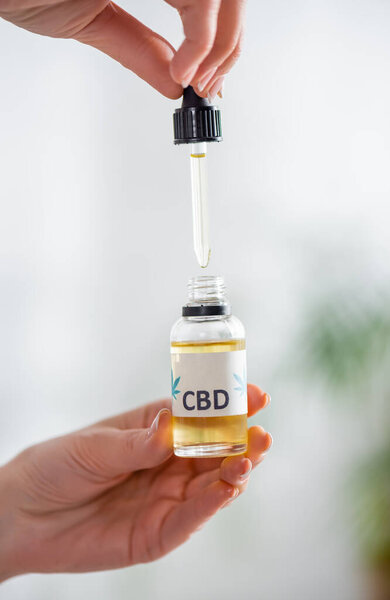 cropped view of mature woman holding pipette and bottle with cbd lettering 