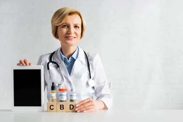 成熟的医生在立方体附近拿着带空白屏幕的数码平板电脑 上面刻有Cbd字母和药物 — 图库照片