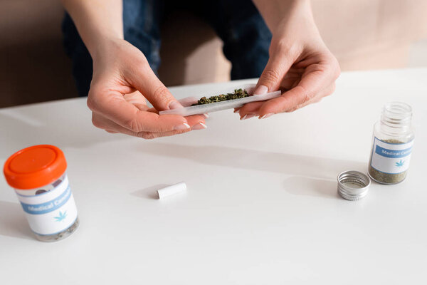 обрезанный вид зрелой женщины, держащей бумагу с сушеной травой рядом с бутылками с медицинскими надписями конопли
 