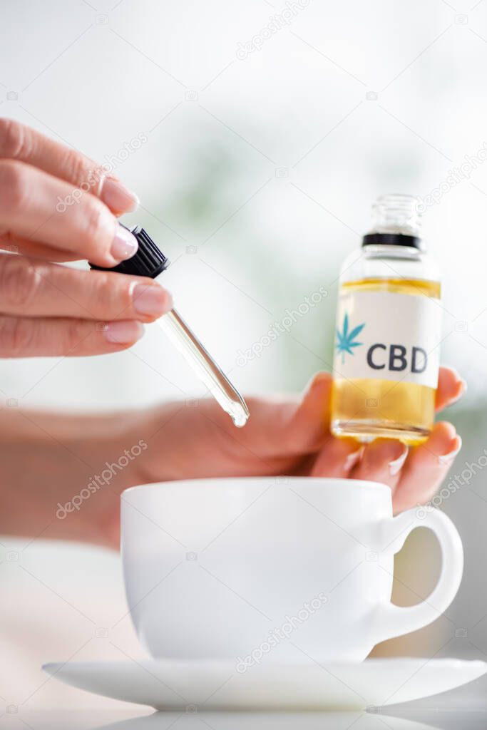 cropped view of mature woman adding drop of cbd in cup of tea 