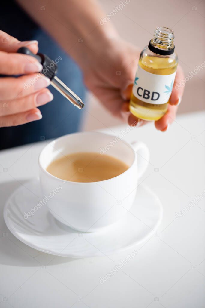 cropped view of mature woman adding cbd in cup of tea on table
