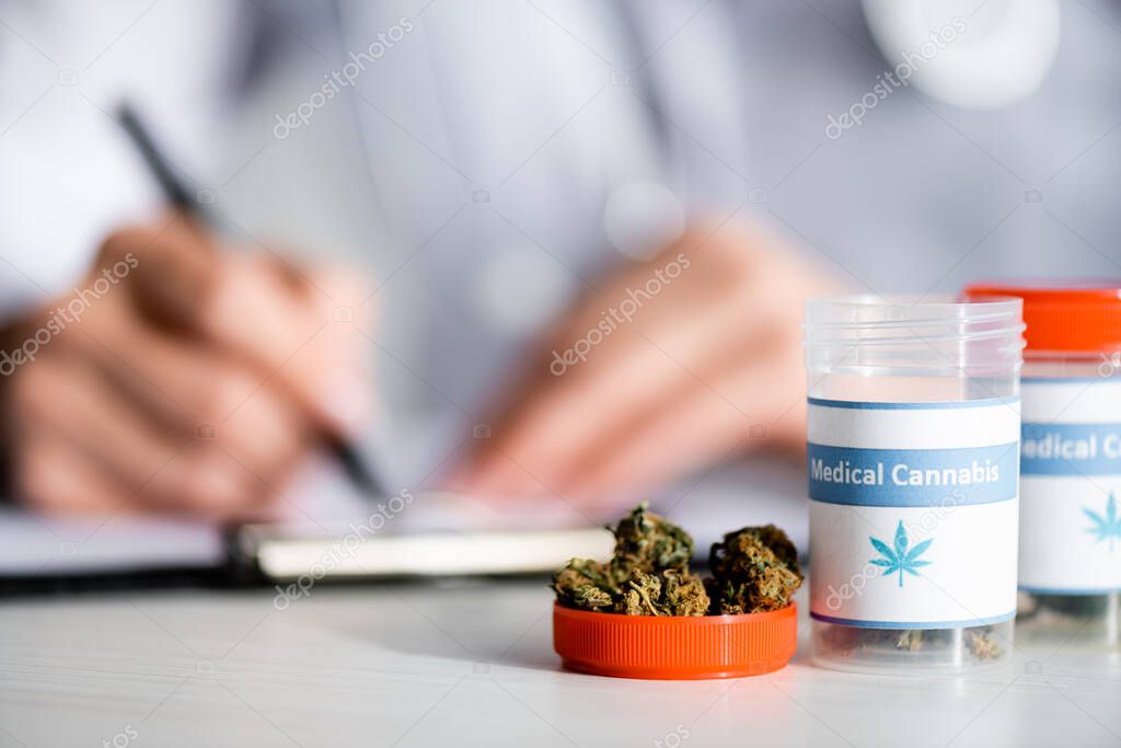 selective focus of dried weed and bottles with medical cannabis lettering near doctor writing prescription 