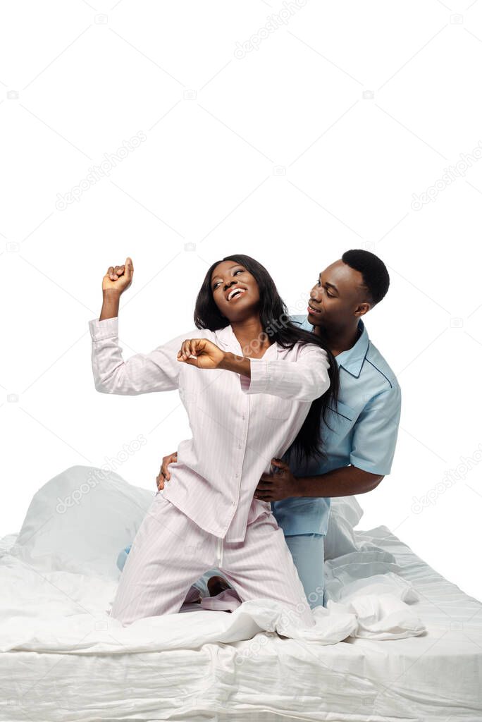 happy african american couple dancing in bed in pajamas isolated on white