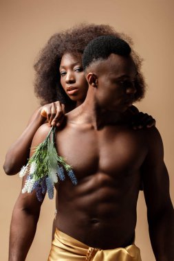 Bej rengi bitkilerle poz veren seksi, çıplak Afrikalı Amerikalı çift.