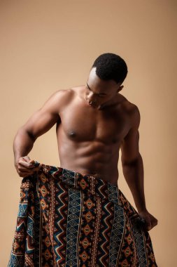 Battaniyeye sarılı seksi, çıplak afro adam bej üzerine izole edilmiş poz veriyor.