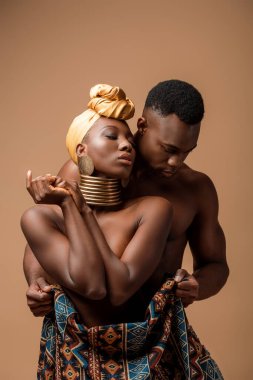 Battaniyeye sarılmış, bej rengi bir erkeğin yanında poz veren seksi, çıplak bir afro kadın.