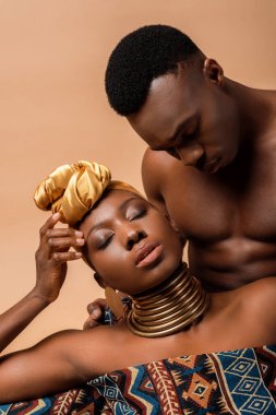 Battaniyeye sarılmış, bej rengi bir erkeğin yanında poz veren seksi, çıplak bir afro kadın.