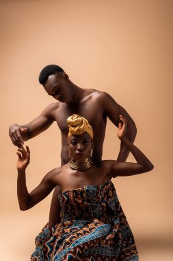 Battaniyeye sarılı seksi çıplak afro kadın bej giyen adamın yanında poz veriyor.
