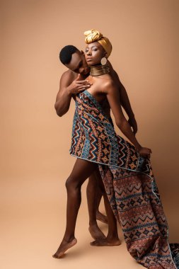 Battaniyeye sarılı seksi çıplak afro kadın bej giyen adamın yanında poz veriyor.