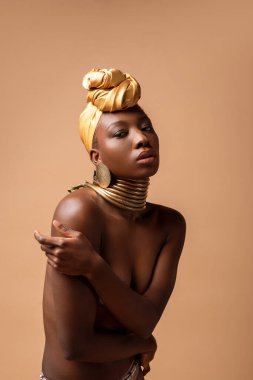 Bej rengi üzerinde yalnız poz veren seksi çıplak afro kadın.
