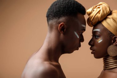 Bej rengi üzerinde yüz yüze poz veren çıplak kabile afro çiftin yan görüntüsü