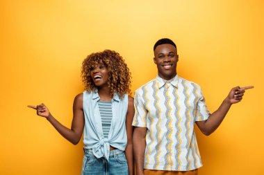 Mutlu Afro-Amerikan çifti sarı renkli arka planı işaret ediyor.
