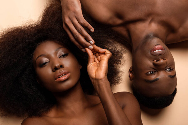 Overhead view of sexy naked african american couple lying with closed eyes on beige