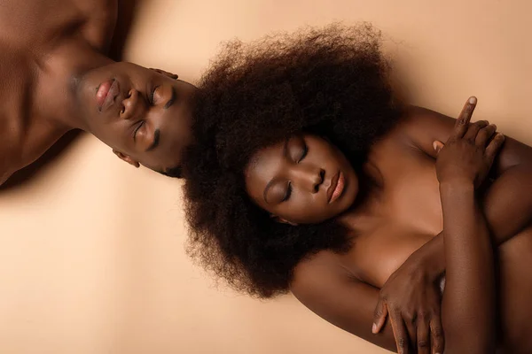 overhead view of sexy naked african american couple lying with closed eyes on beige