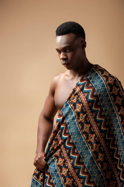 sexy naked tribal afro man covered in blanket posing isolated on beige