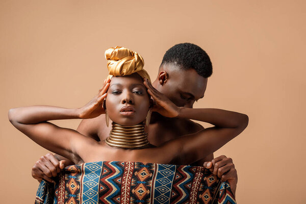Sexy naked tribal afro woman covered in blanket posing near man isolated on beige