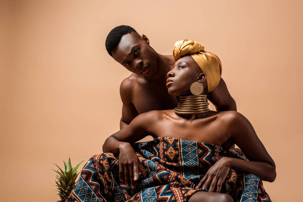 sexy naked tribal afro woman covered in blanket posing near man on beige