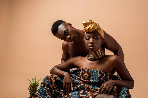 Battaniyeye sarılı seksi çıplak afro kadın bej giyen adamın yanında poz veriyor.