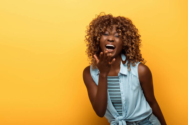 happy african american woman laughing on yellow background