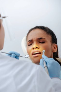 Lateks eldivenli ortodontist seçici odak, diş teli takmış üzgün Afrikalı Amerikalı bir kadının yanında diş aletleri tutuyor. 