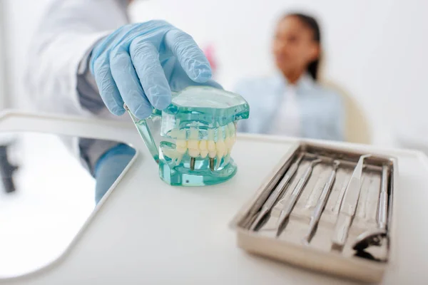歯科器具の近くで歯モデルを取るラテックス手袋の歯科医の選択焦点 — ストック写真