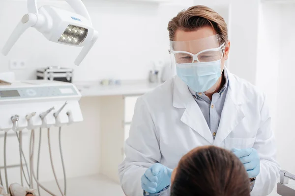 牙科医生在妇女近旁戴面罩 医用面罩和乳胶手套的选择焦点 — 图库照片