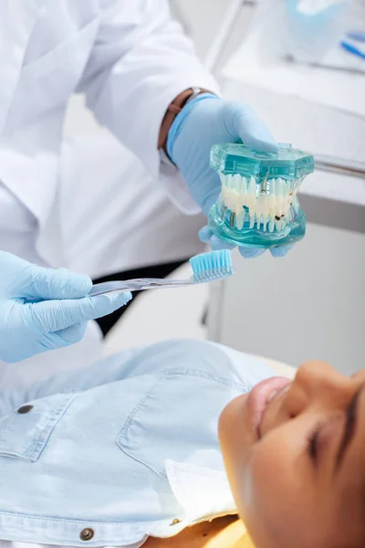 幸せなアフリカ系アメリカ人患者の近くに歯モデルと歯ブラシを持つ歯科医の選択的焦点 — ストック写真
