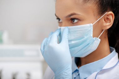 Afro-Amerikan diş hekimi klinikte maske takıyor. 