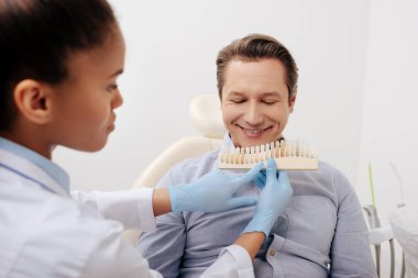 Seçici odak noktası Afrika kökenli Amerikalı dişçinin klinikte mutlu bir hastanın yanında diş paleti tutması. 
