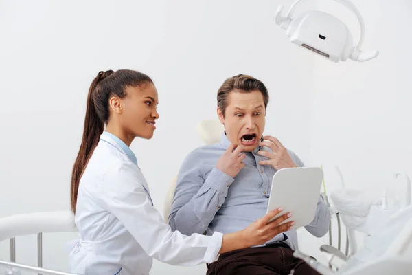 Τρομοκρατημένος Ασθενής Κοιτάζεται Στον Καθρέφτη Κοντά Στον Χαρούμενο Αφροαμερικανό Οδοντίατρο — Φωτογραφία Αρχείου