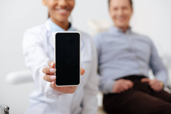 selective focus of cheerful african american dentist holding smartphone with blank screen near happy patient 