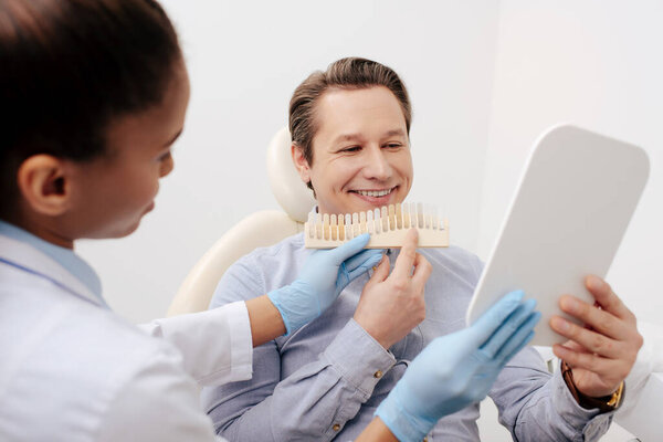selective focus of african american dentist holding teeth palette near cheerful patient looking at mirror