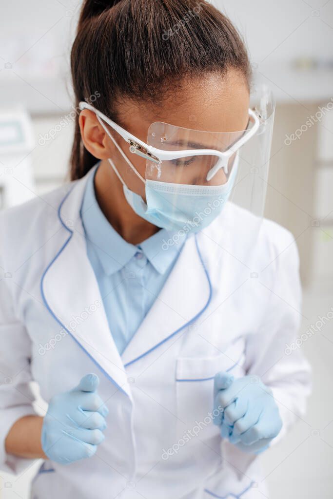 african american dentist in medical mask, face shield and latex gloves 