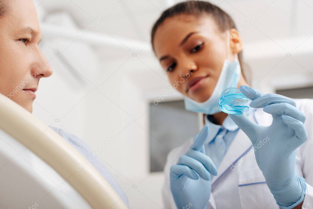 selective focus of african american dentist in latex gloves pointing with finger at retainer near patient 