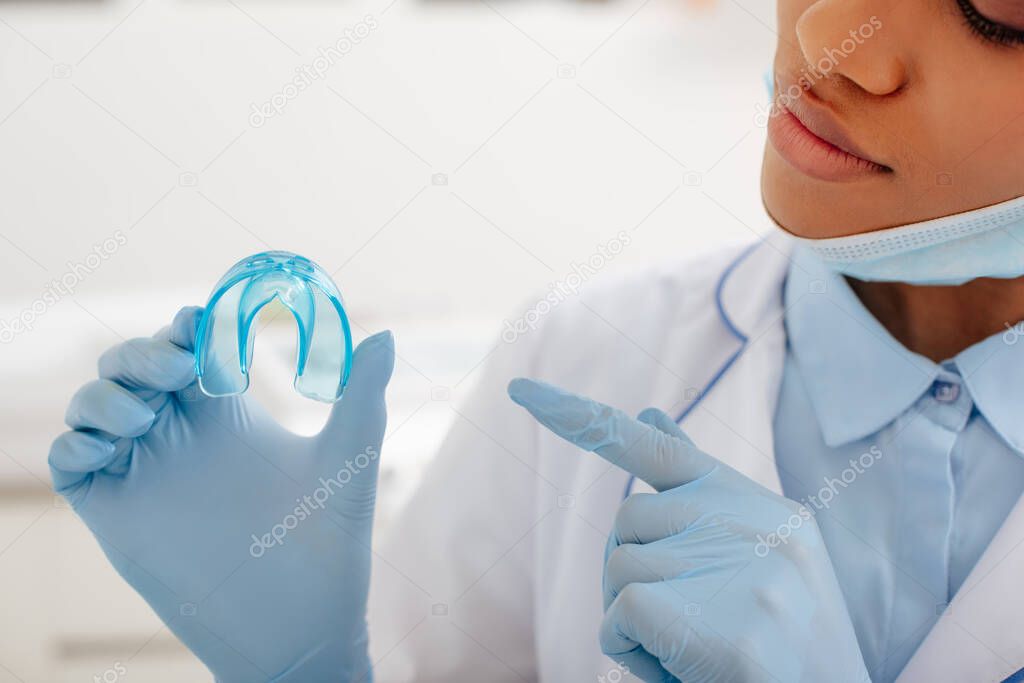 cropped view of african american dentist pointing with finger at retainer 